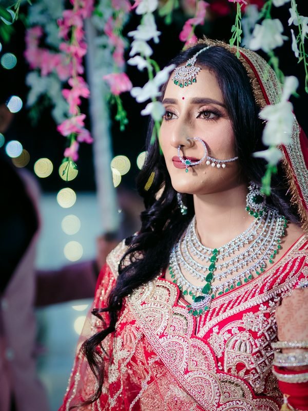 Bride under a floral phoolon ki chaadar with diamond and emerald jewellery, makeup by THE HBM