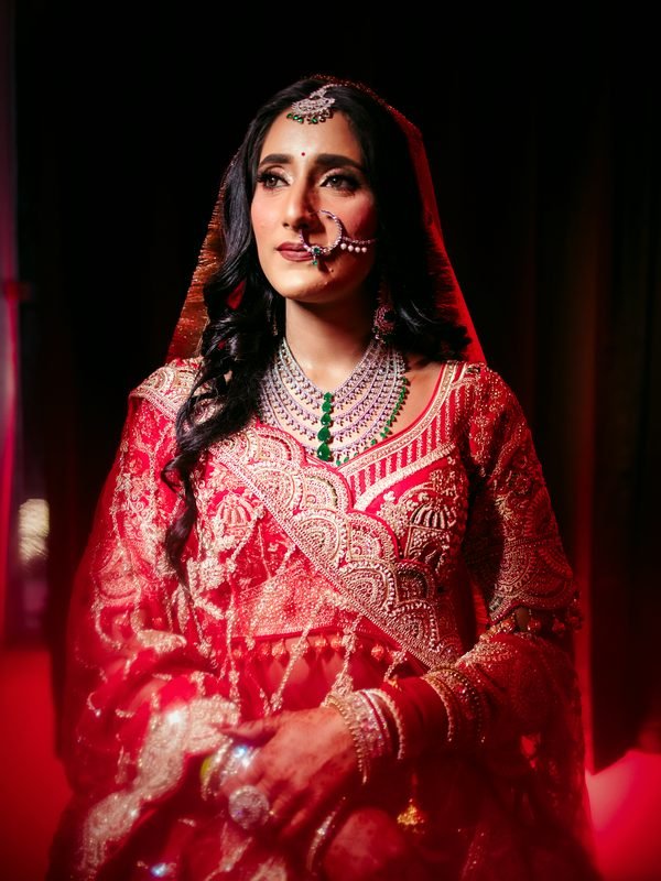 Bride in red embroidered lehenga with diamond and emerald jewellery, makeup by THE HBM